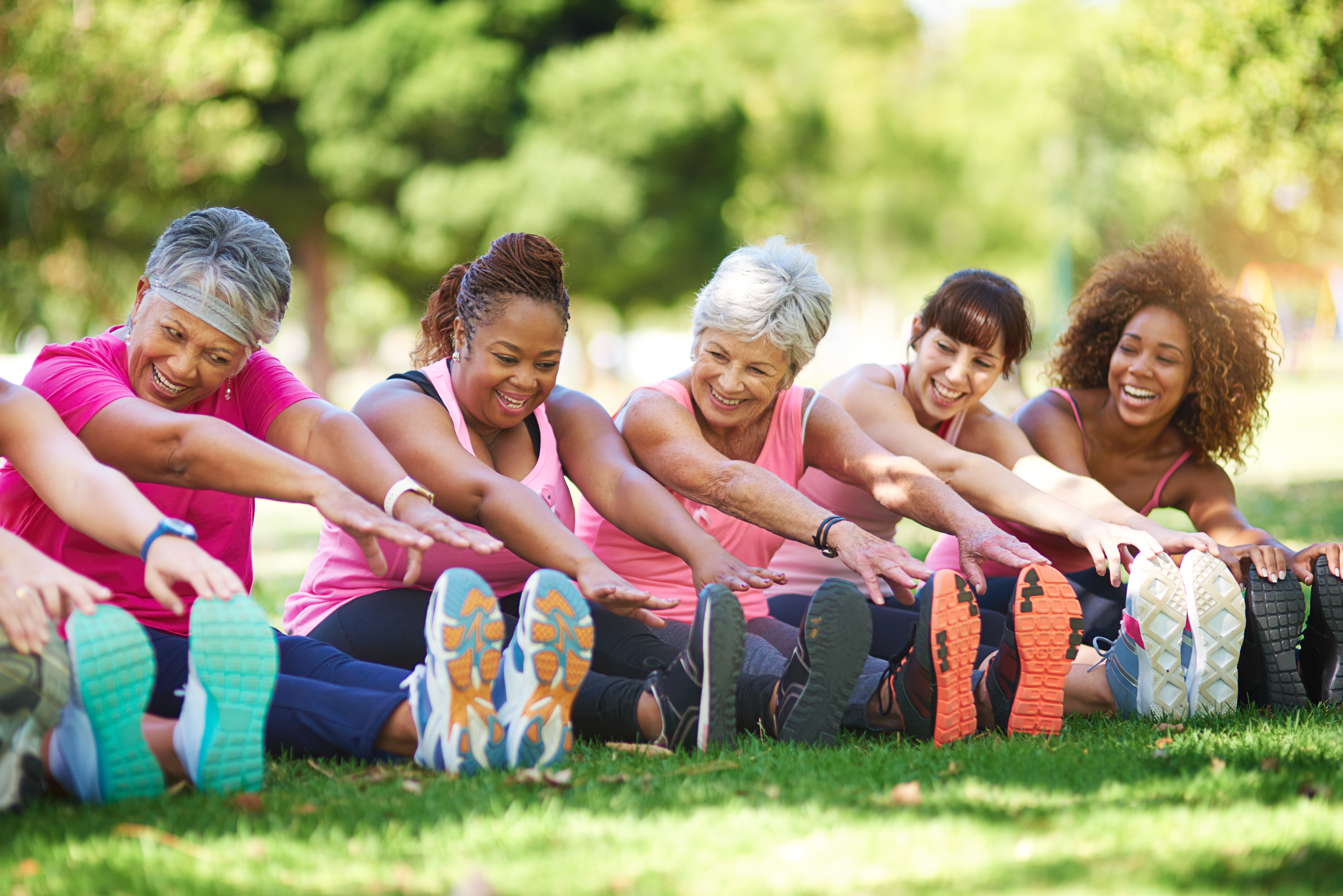 Group of older women stretching on grass, smiling